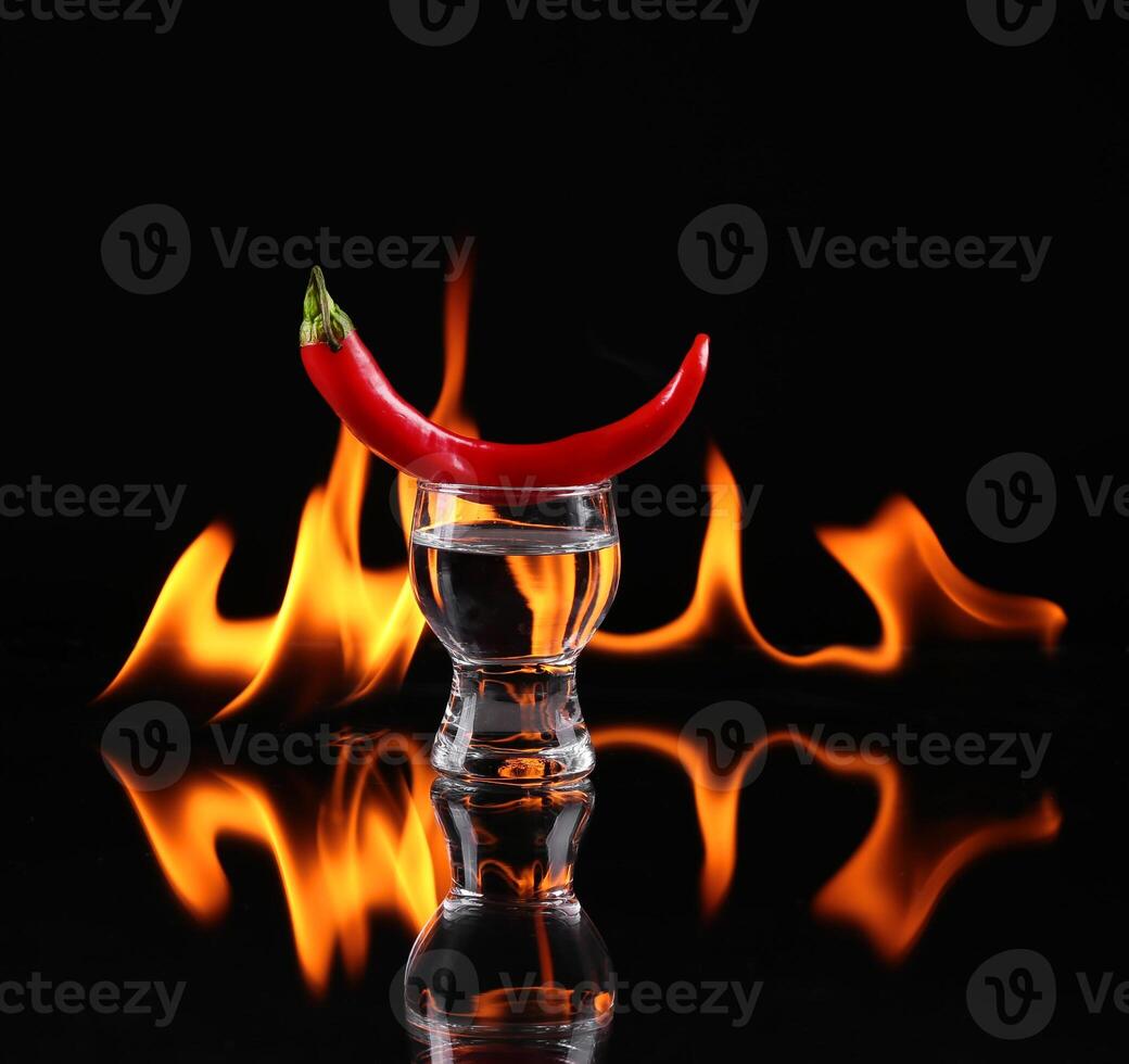 Hot chili pepper in a shot glass with a fire on a black background photo