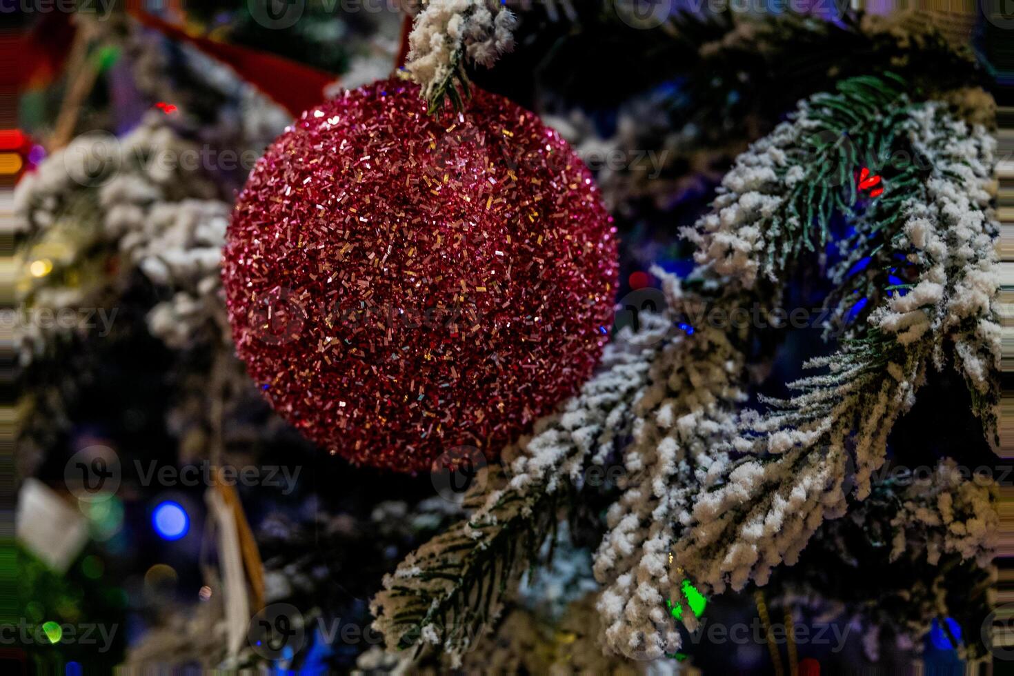 A sparkling red ornament hangs from a Christmas tree branch adorned with artificial snow. photo