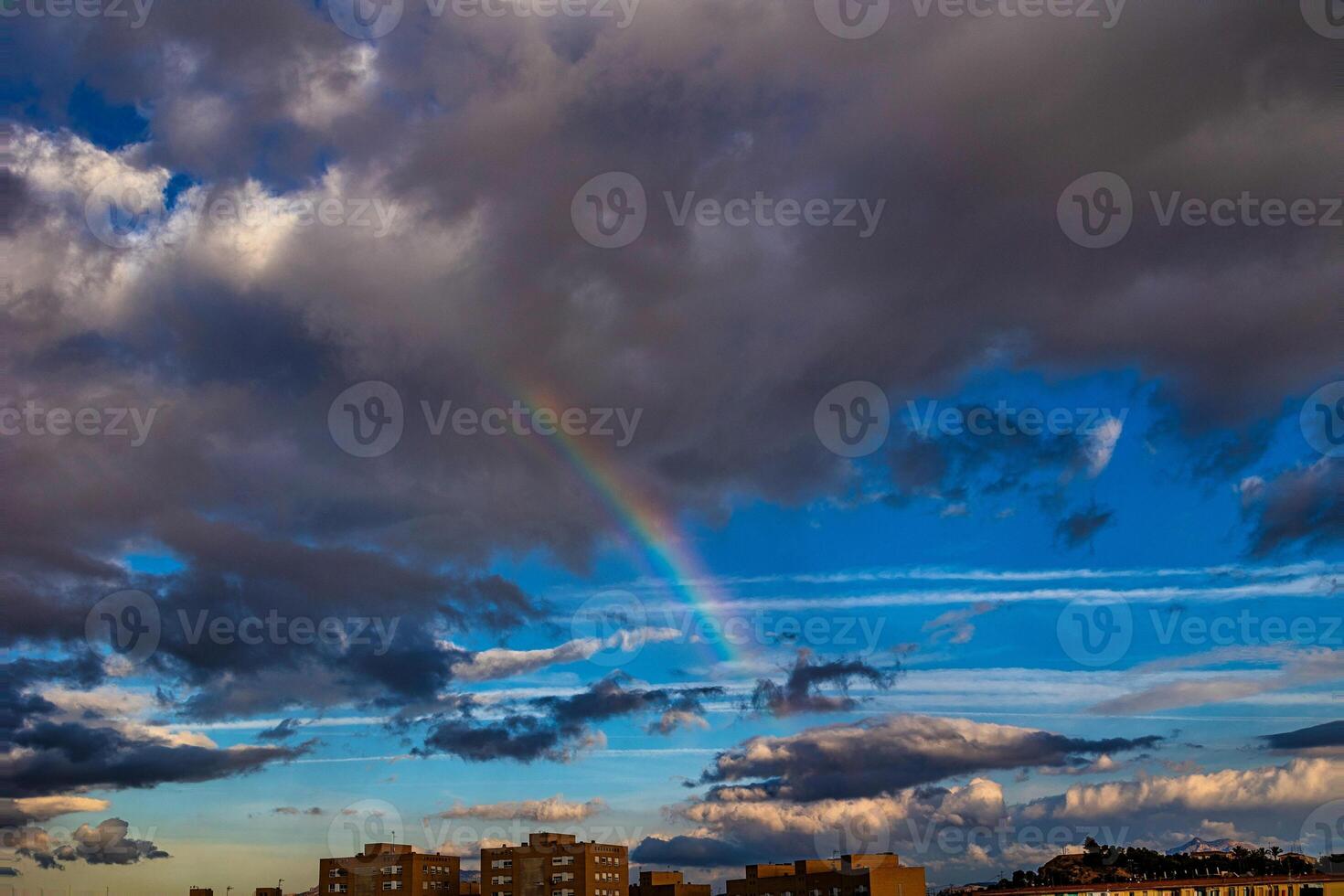 A colorful rainbow arcs across a dramatic sky filled with dark and light clouds photo