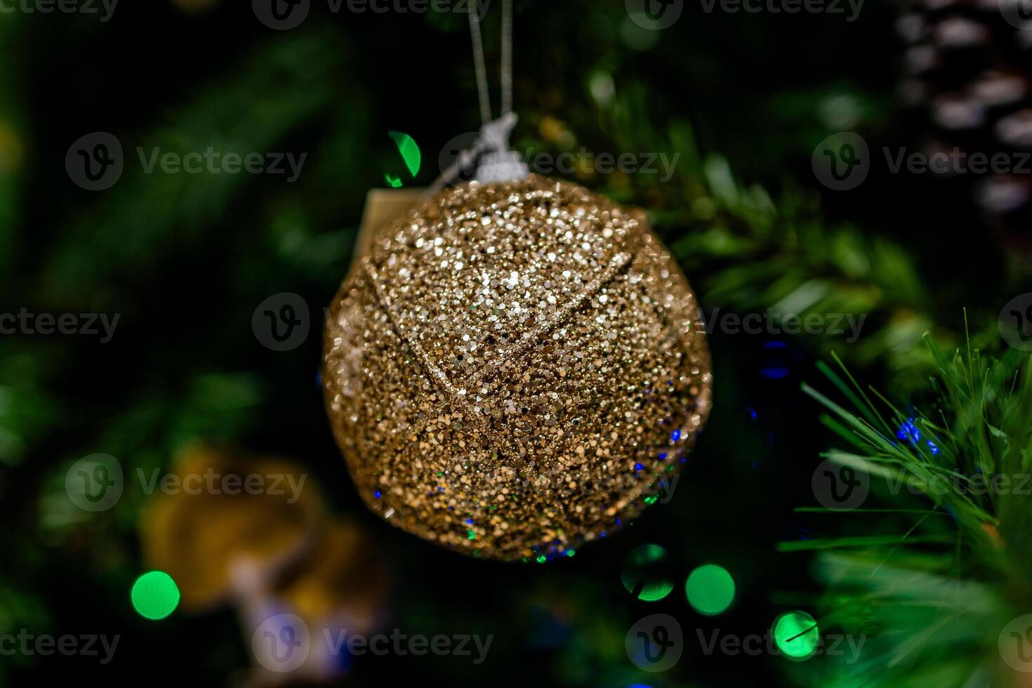 A glittering gold ornament hangs from a festive, green Christmas tree photo