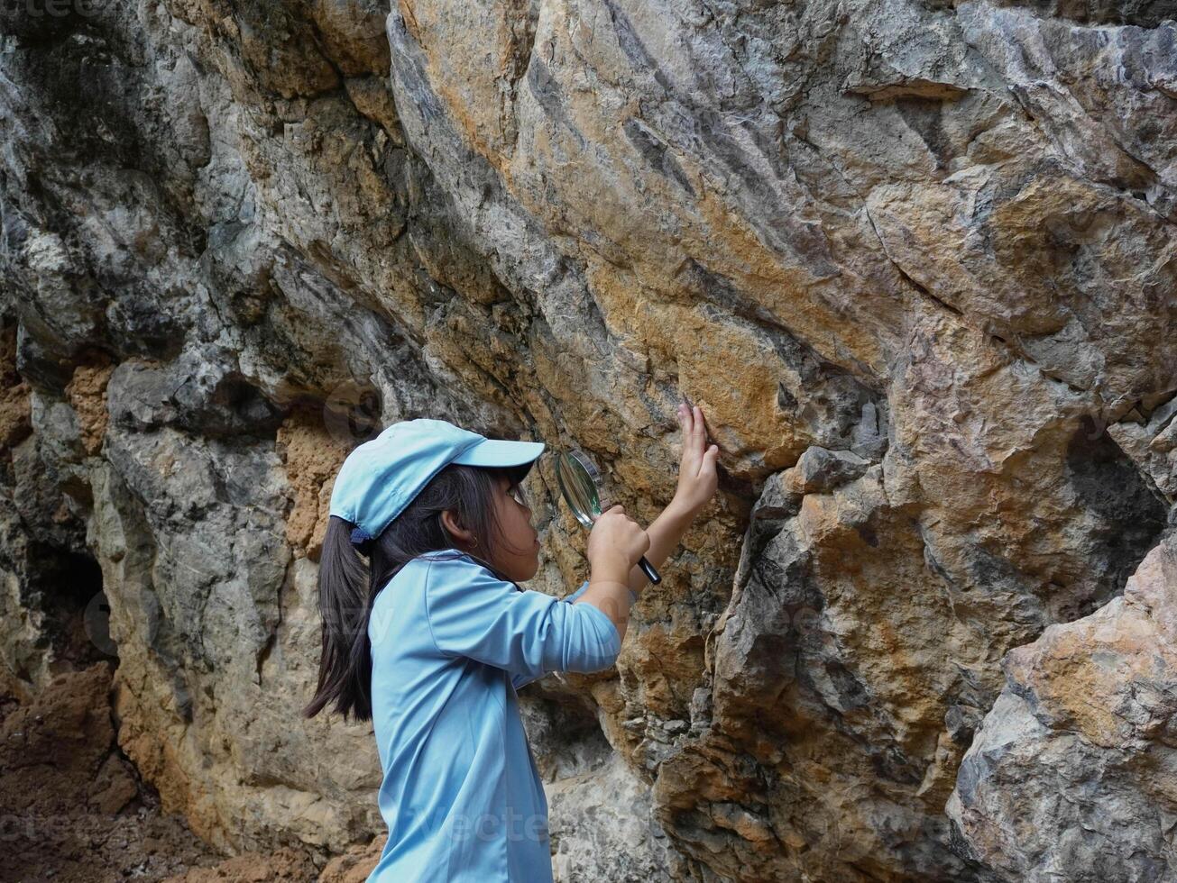 A girl examines rocks through a magnifying glass while exploring the nature of a forest on a sunny day. Outdoor ecology school lesson. photo
