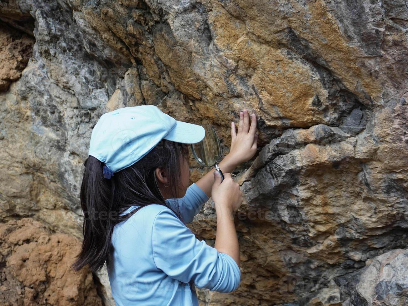 A girl examines rocks through a magnifying glass while exploring the nature of a forest on a sunny day. Outdoor ecology school lesson. photo