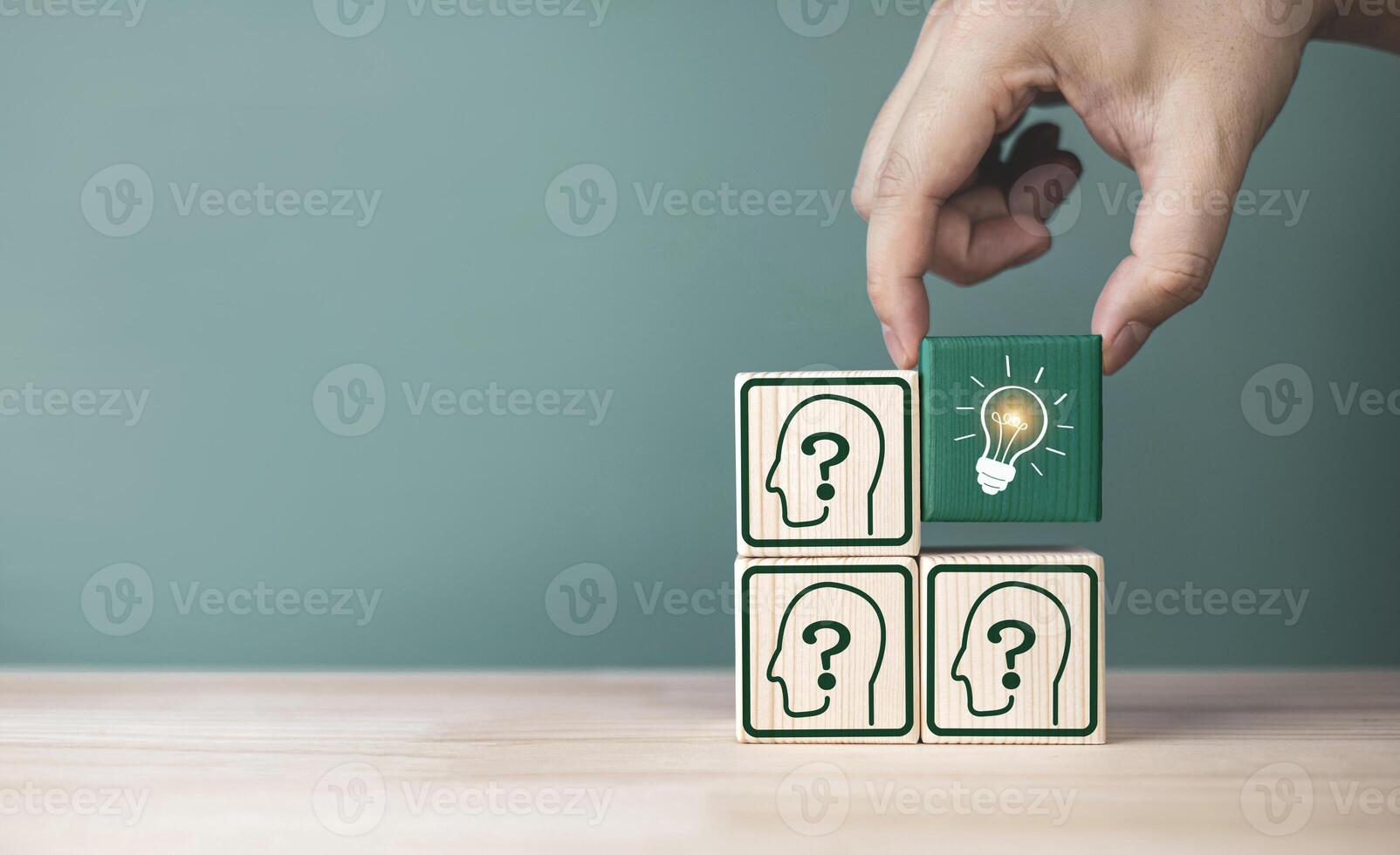 A hand picks up light bulb icon inside a wooden block placed around a human icon with question. Concept of seeking knowledge, intelligent problem solving, good ideas, and new innovation. photo