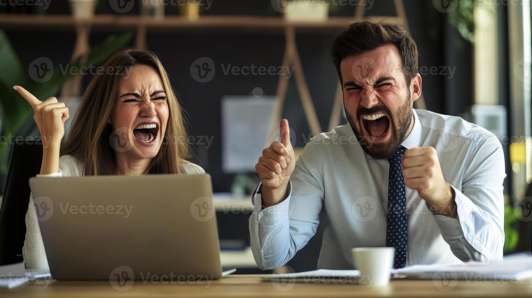 A man and a woman are sitting at a desk with a computer monitor in front of them. The man is smiling and holding his hands up in the air, while the woman is also smiling. Scene is happy and positive. photo