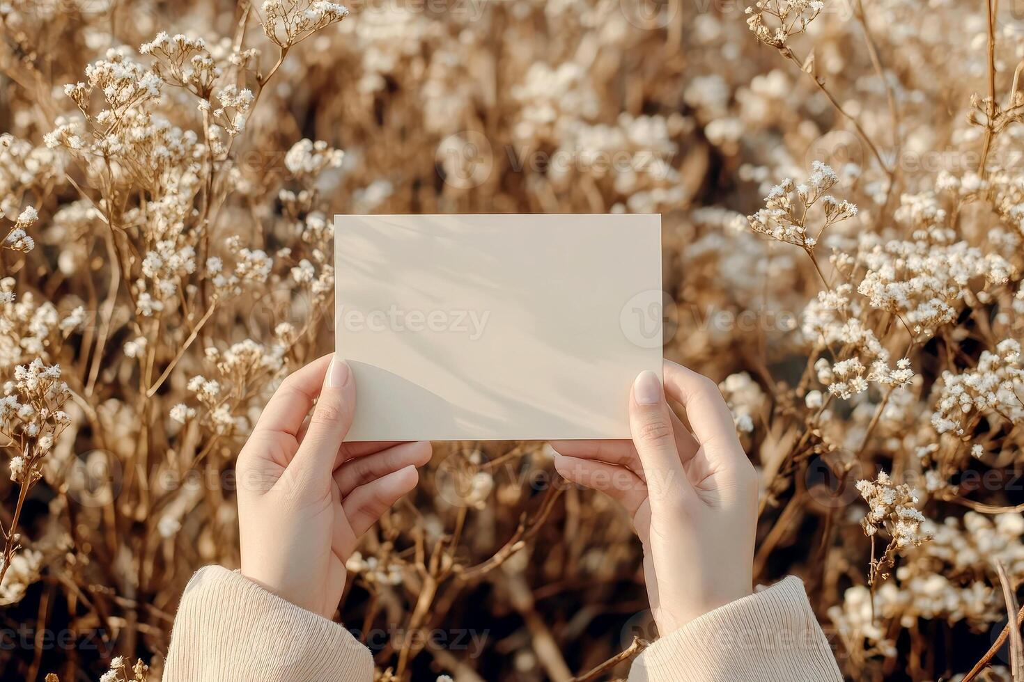 Hand holding printed greeting card mock up, blank empty postcard isolated on natural flower background photo