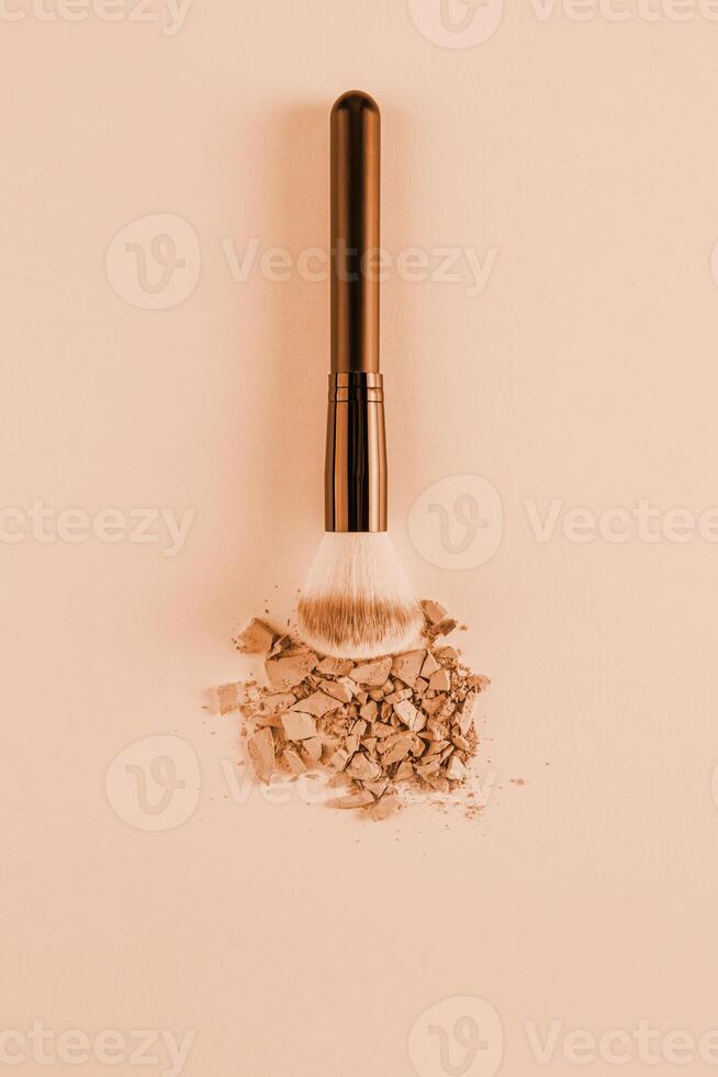 A sample of dry compact powder in a beige tone, pieces of powder and a chic fluffy cosmetic brush on a beige background. vertical view. A copy space. photo