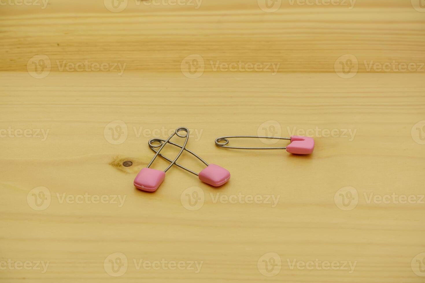 One open and one closed safety pin with pink caps lie on a wooden background. photo