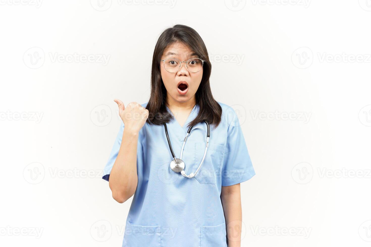Showing and Pointing Product With Thumb Of Asian Young Doctor Isolated On White Background photo