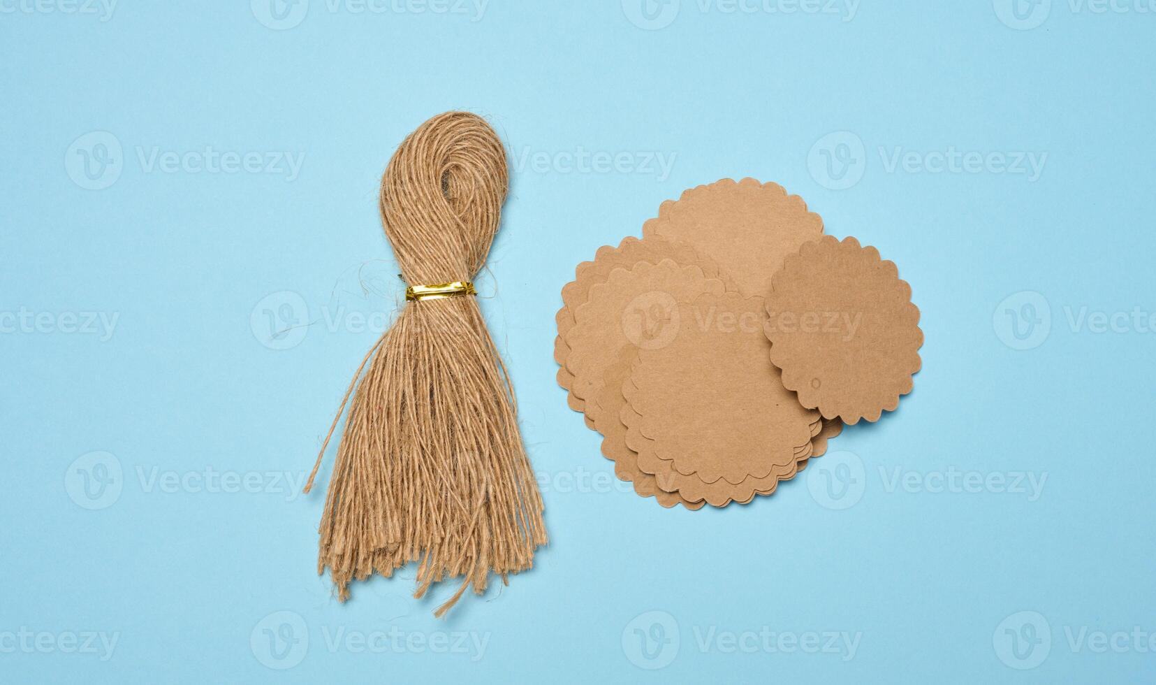 Bundle of brown rope and round paper tags on blue background, top view photo