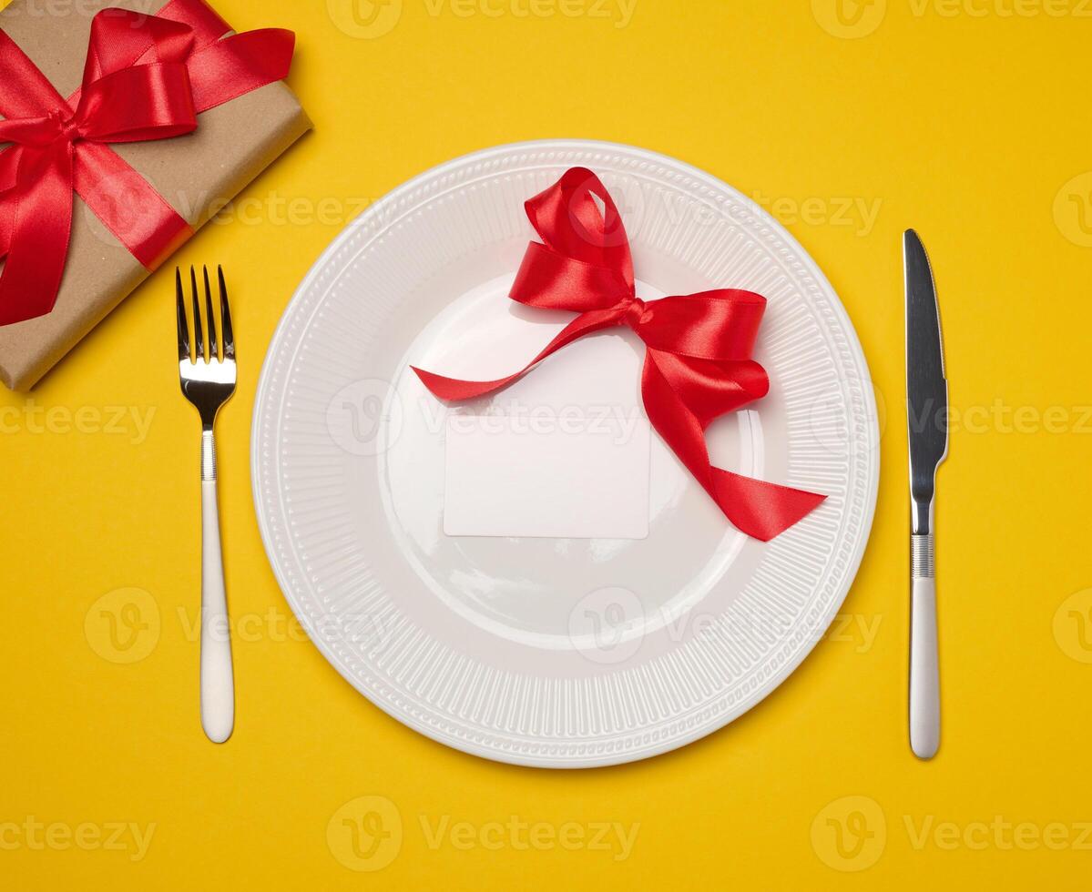 Blank white paper business card lies in a round plate on a yellow background, top view photo
