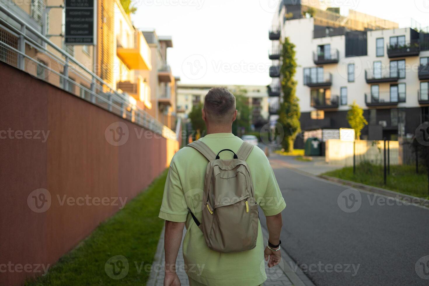 Back view of Caucasian man with blonde hair and backpack walking on street of Krakow city photo
