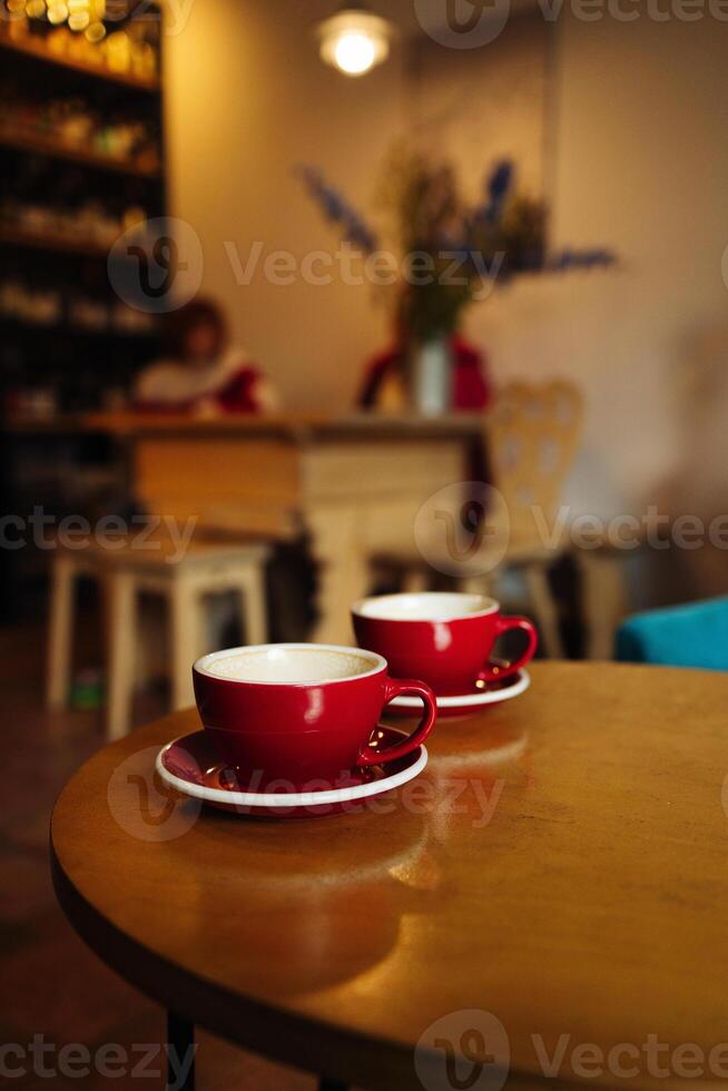 Two red cups of coffee with milk with trendy heart shape latte art. Drinking coffee on the terrace. photo