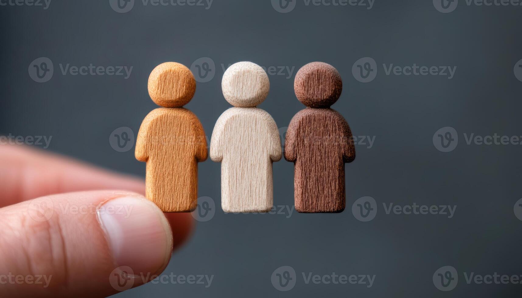 A hand holds three wooden figures representing different skin tones, showcasing diversity photo