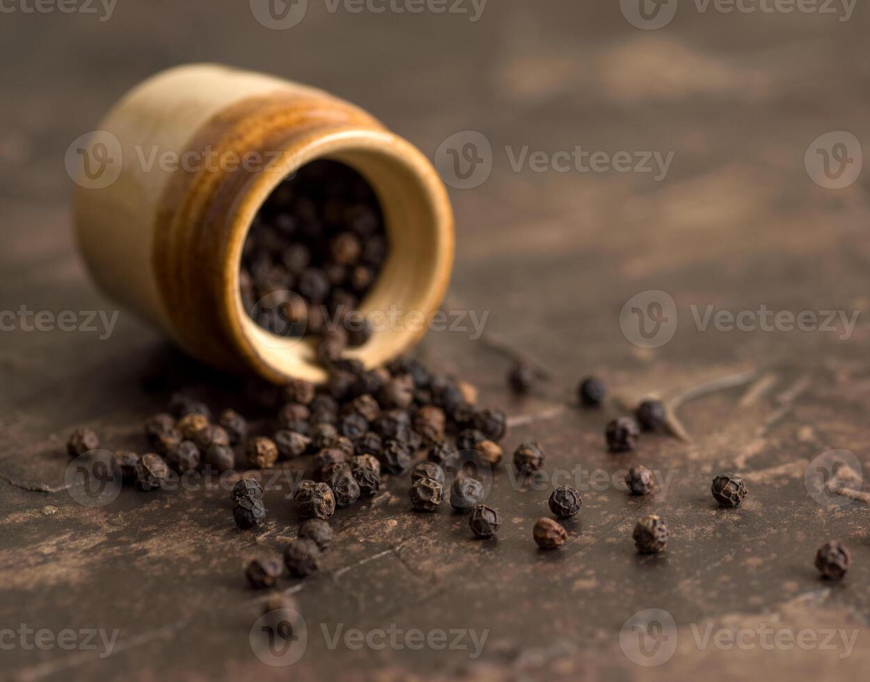 Close up of black pepper or peppercorns with a clay pot on a stone background. photo