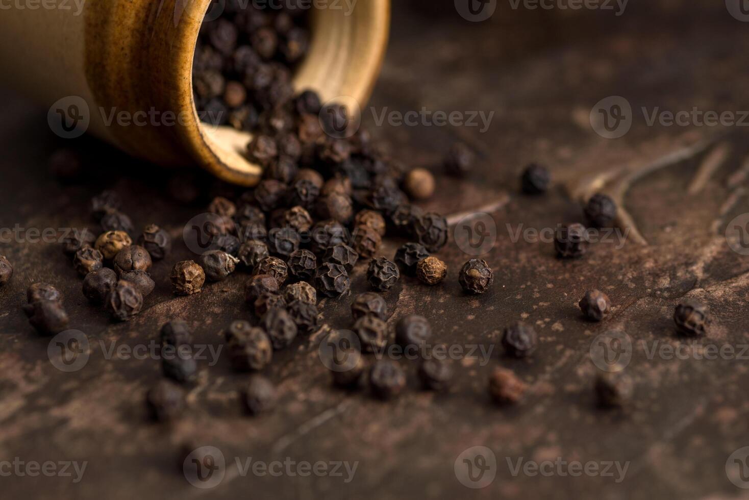 Close up of black pepper or peppercorns with a clay pot on a stone background. photo