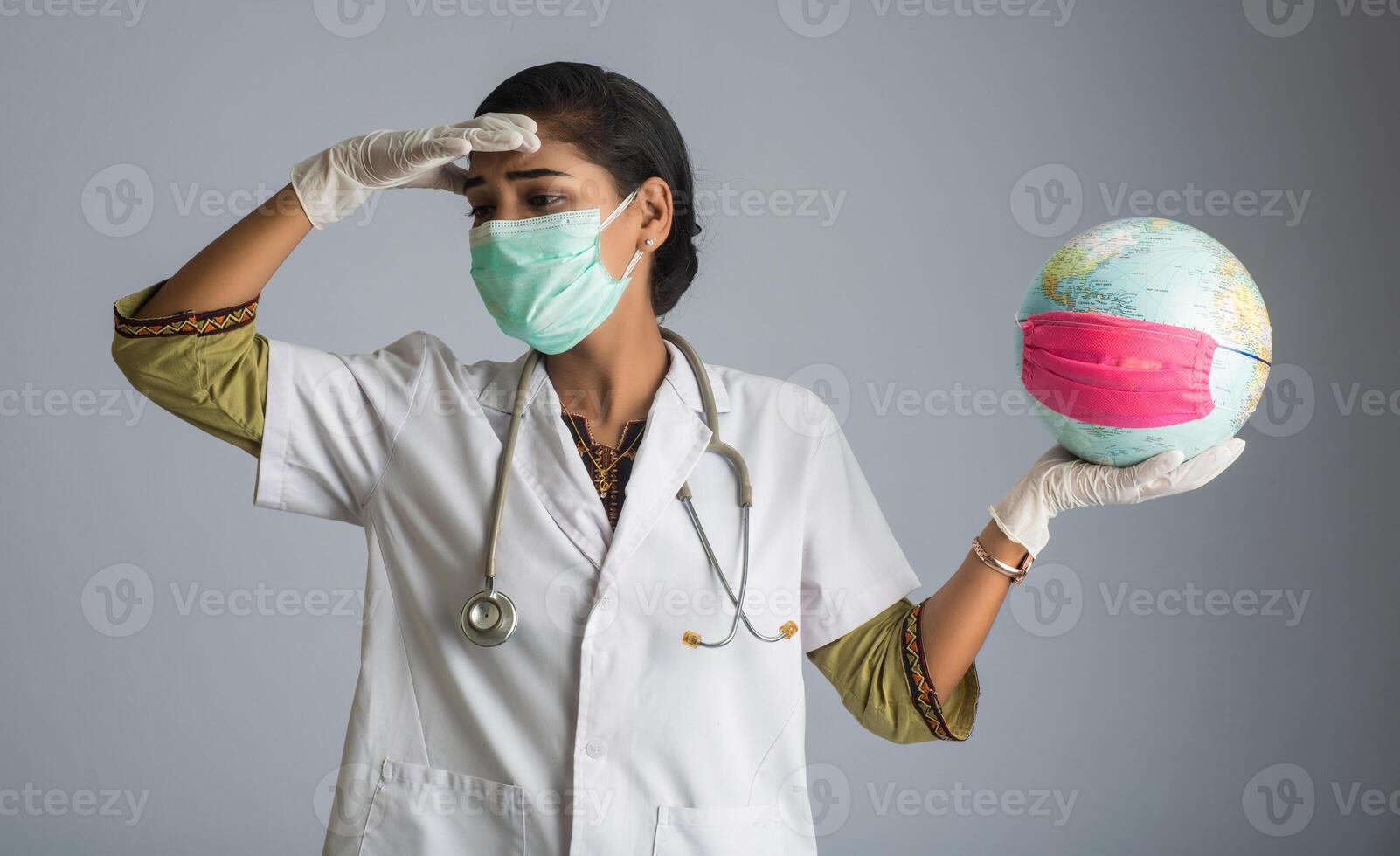 Woman doctor holding world globe with a medicine face mask feeling sick or ill. World epidemic of coronavirus concept. photo