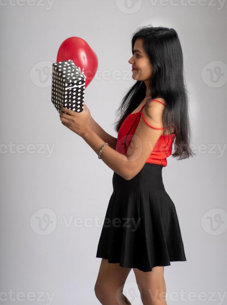 Cheerful cute girl in fancy red and black outfit posing with heart shape balloon and gift box. photo