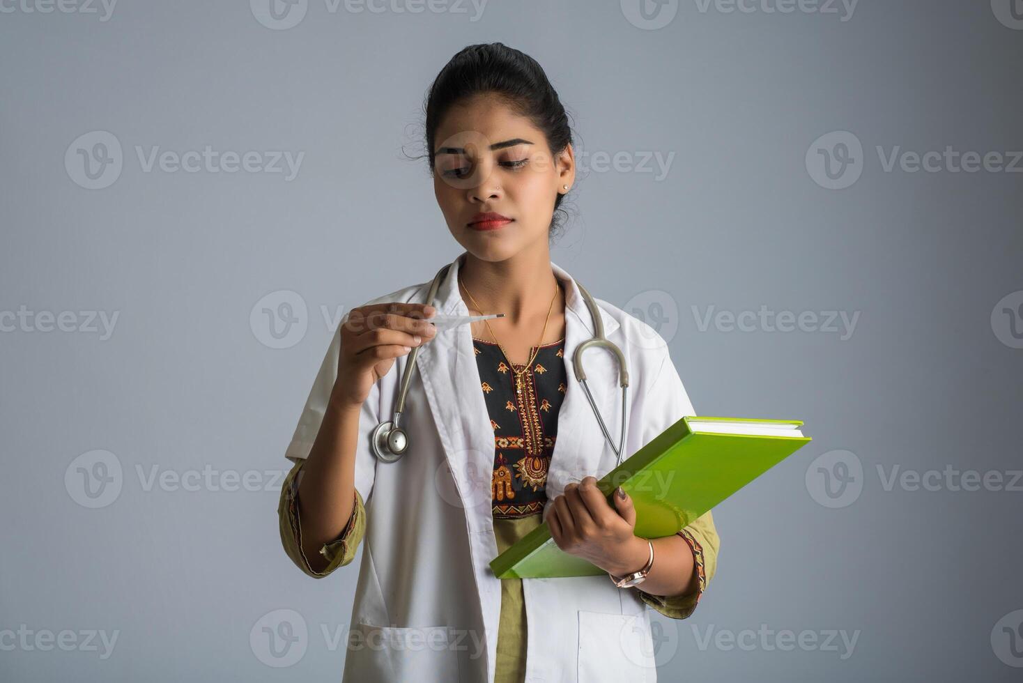 Beautiful young woman doctor with thermometer and report or book photo