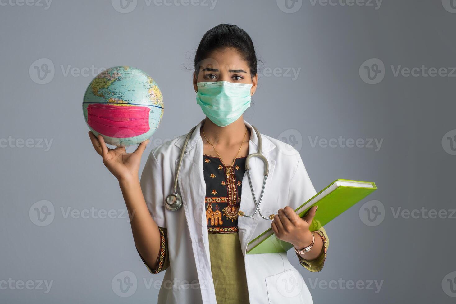 Woman doctor holding world globe and book or report with a medical face mask. World epidemic of coronavirus concept. photo