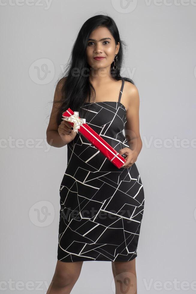 Portrait of a pretty young girl posing with gift box on grey background. photo