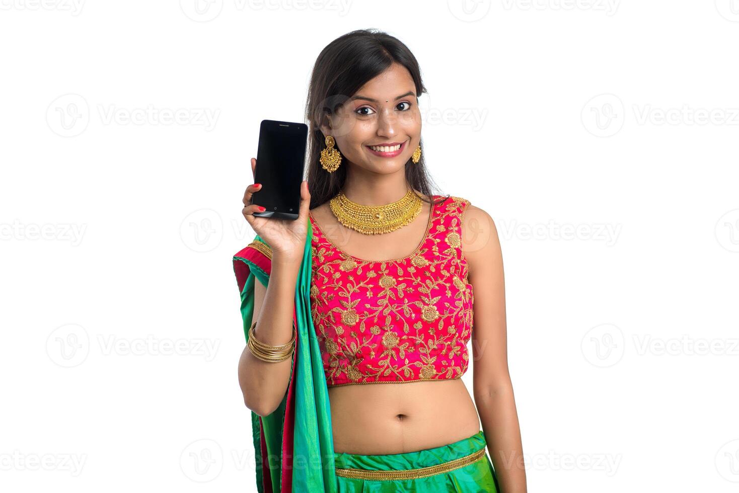 Young Indian traditional girl using a mobile phone or smartphone and showing blank screen smart phone on white background photo