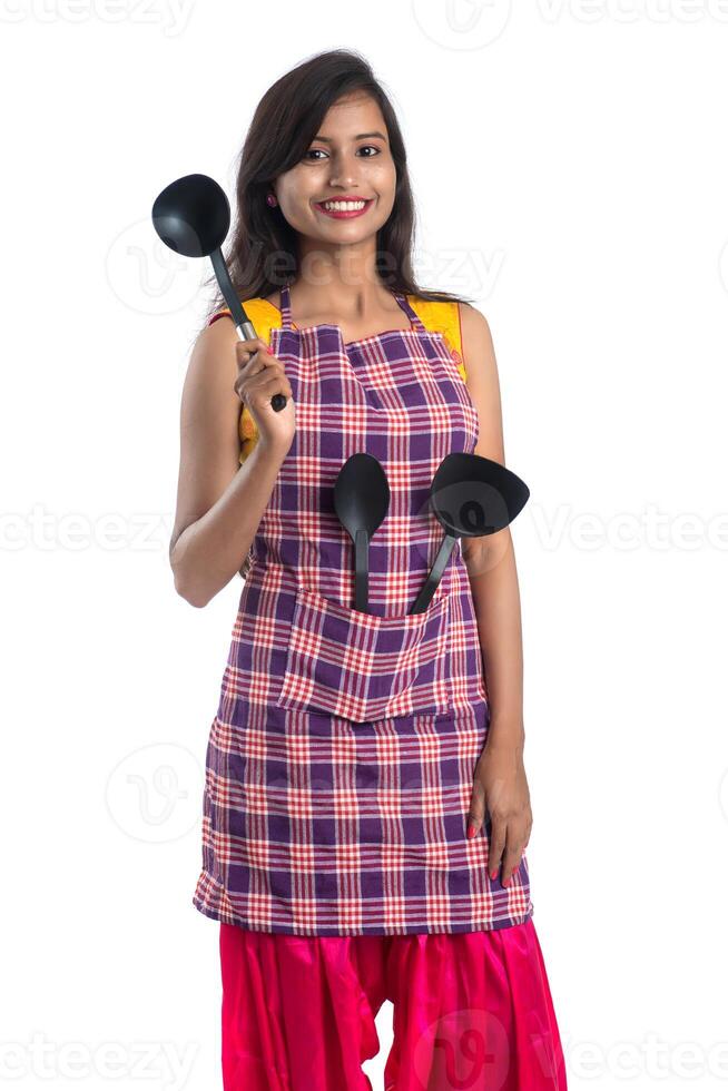 Joven india sosteniendo una cuchara de utensilios de cocina, stapula, cucharón y sartén, etc. sobre un fondo blanco. foto