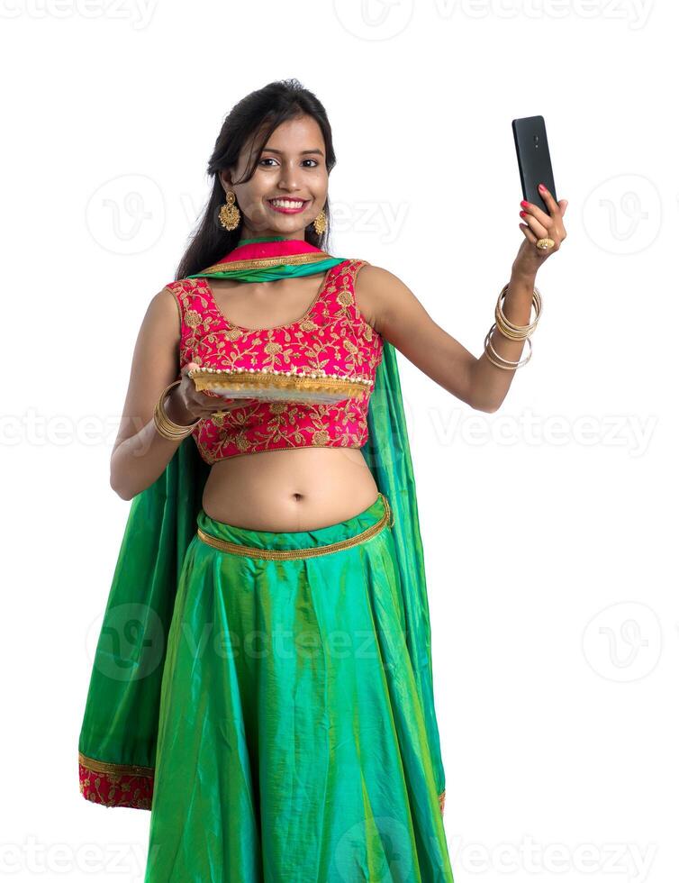 Beautiful young happy girl taking a selfie with clay lamp or diya during the festival of light Diwali using a smartphone on a white background photo