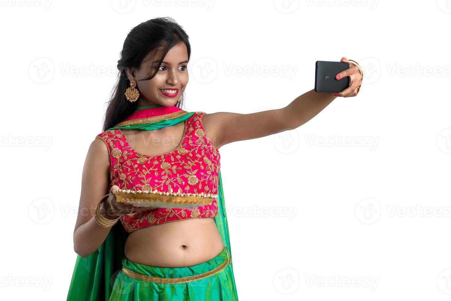 Beautiful young happy girl taking a selfie with clay lamp or diya during the festival of light Diwali using a smartphone on a white background photo