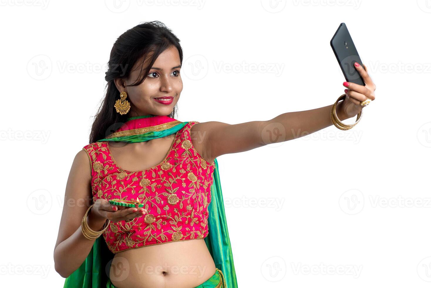 Beautiful young happy girl taking a selfie with clay lamp or diya during the festival of light Diwali using a smartphone on a white background photo