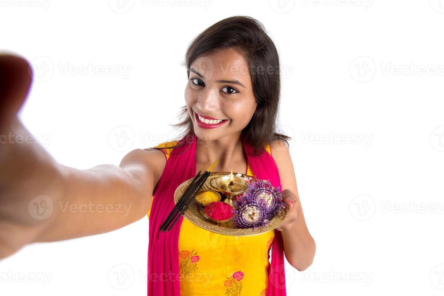 Beautiful young happy girl taking selfie with pooja thali using a mobile phone or smartphone on a white background photo