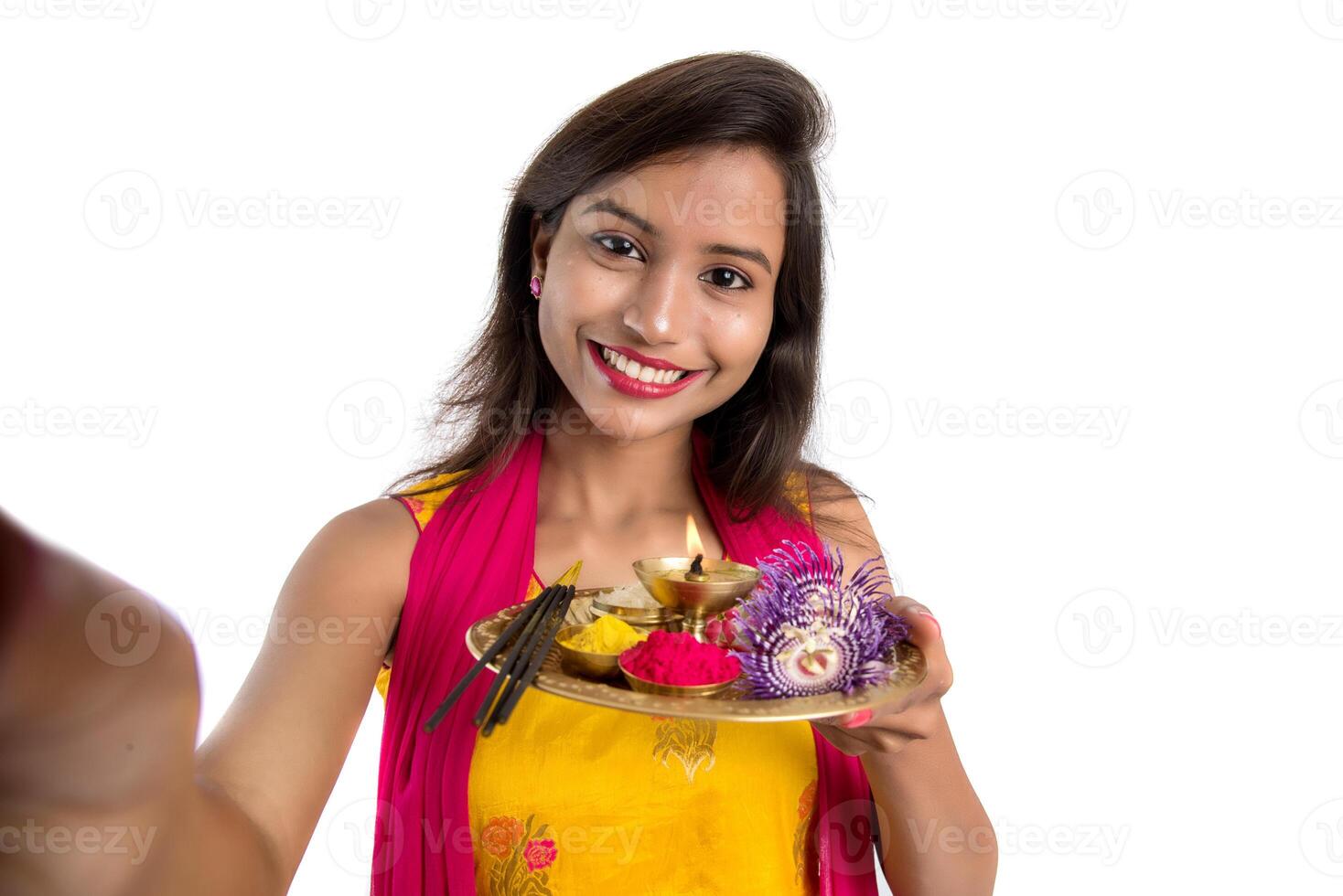 Beautiful young happy girl taking selfie with pooja thali using a mobile phone or smartphone on a white background photo