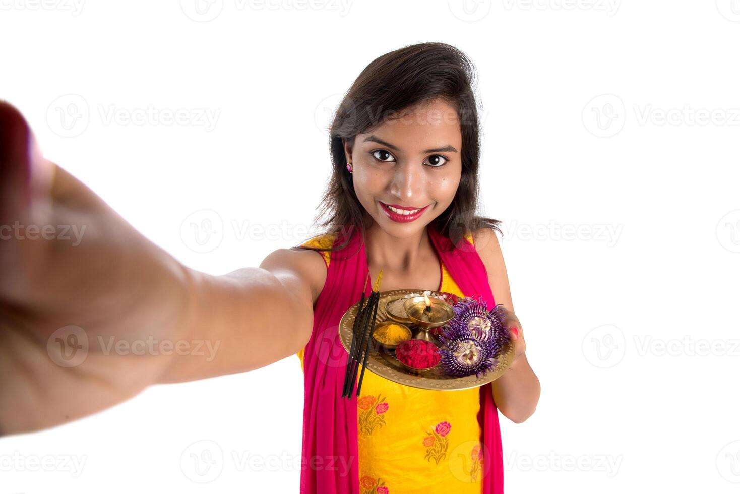 Beautiful young happy girl taking selfie with pooja thali using a mobile phone or smartphone on a white background photo