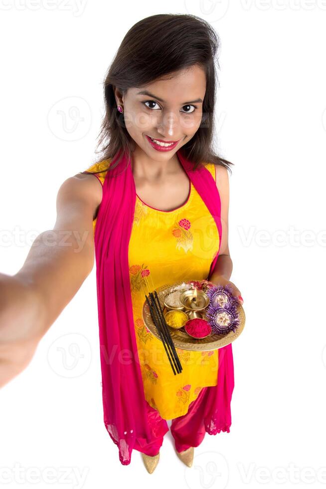Beautiful young happy girl taking selfie with pooja thali using a mobile phone or smartphone on a white background photo