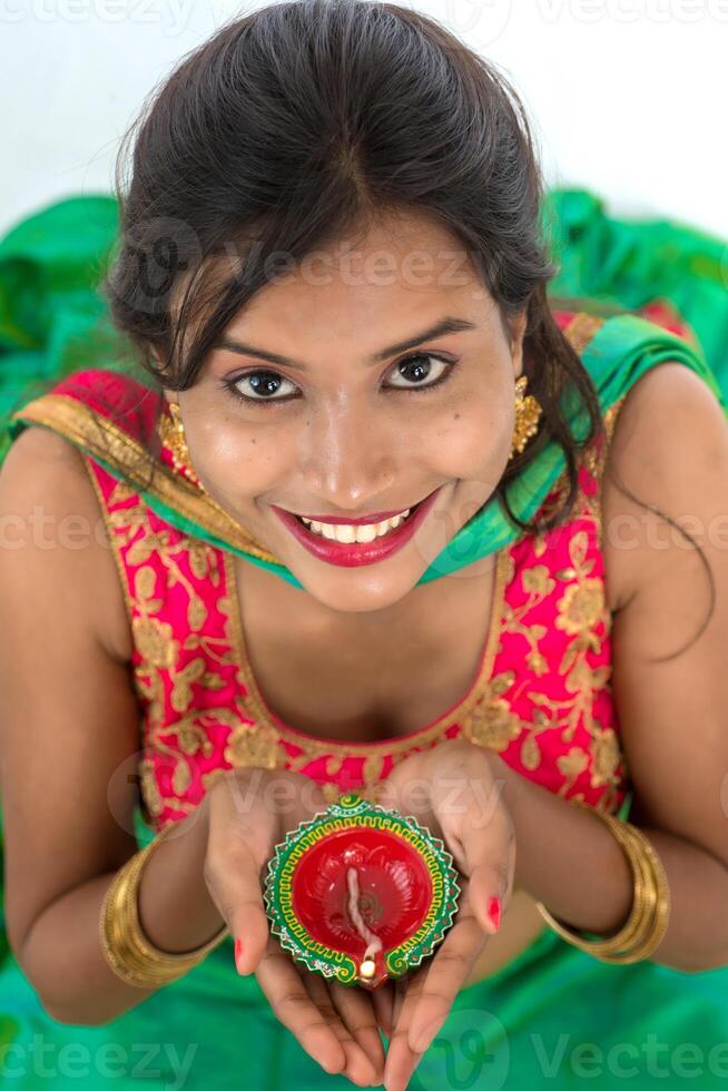 Portrait of a Indian Traditional Girl holding Diya, Girl Celebrating Diwali or Deepavali with holding oil lamp during festival of light on white background photo