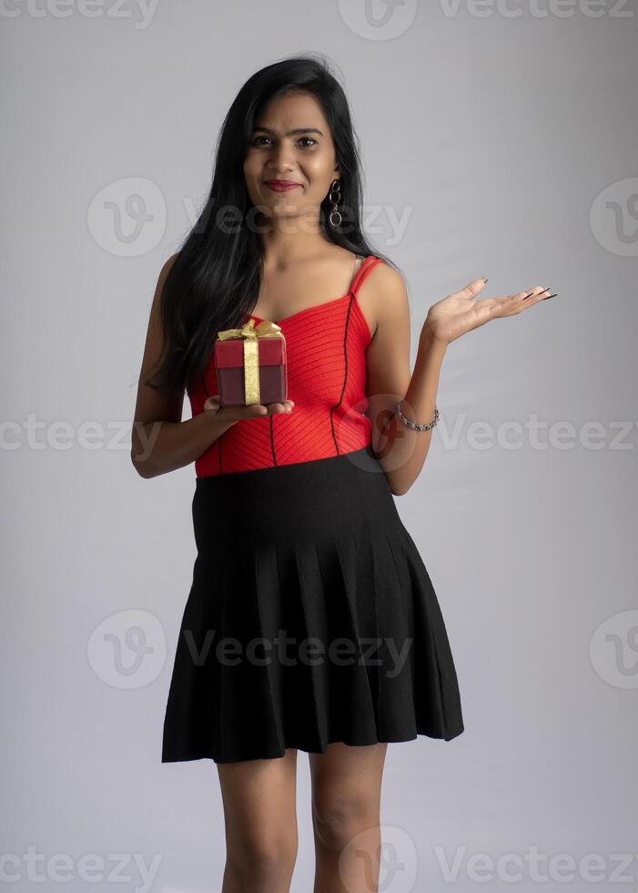 Portrait of a pretty girl holding and posing with gift box on grey background photo