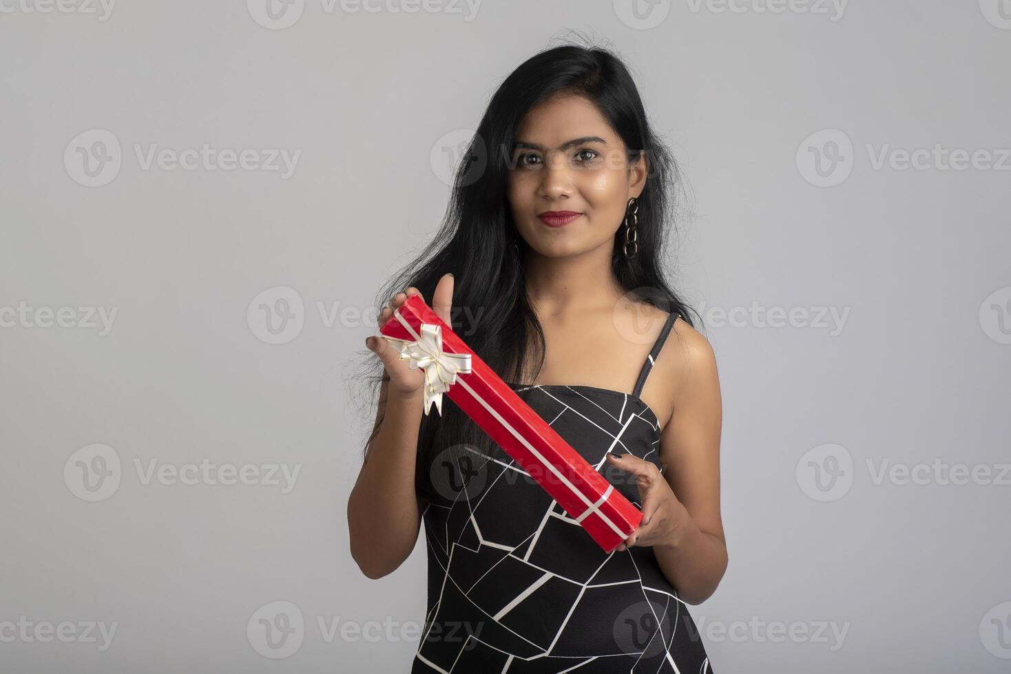Portrait of a pretty young girl posing with gift box on grey background. photo