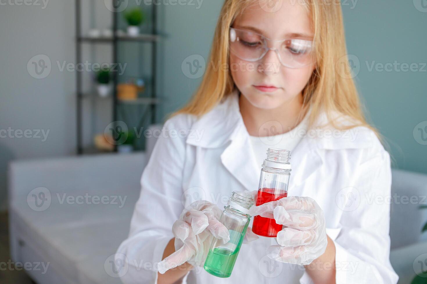 The girl conducts chemical experiments at home. Focus on flasks with colored liquid. photo