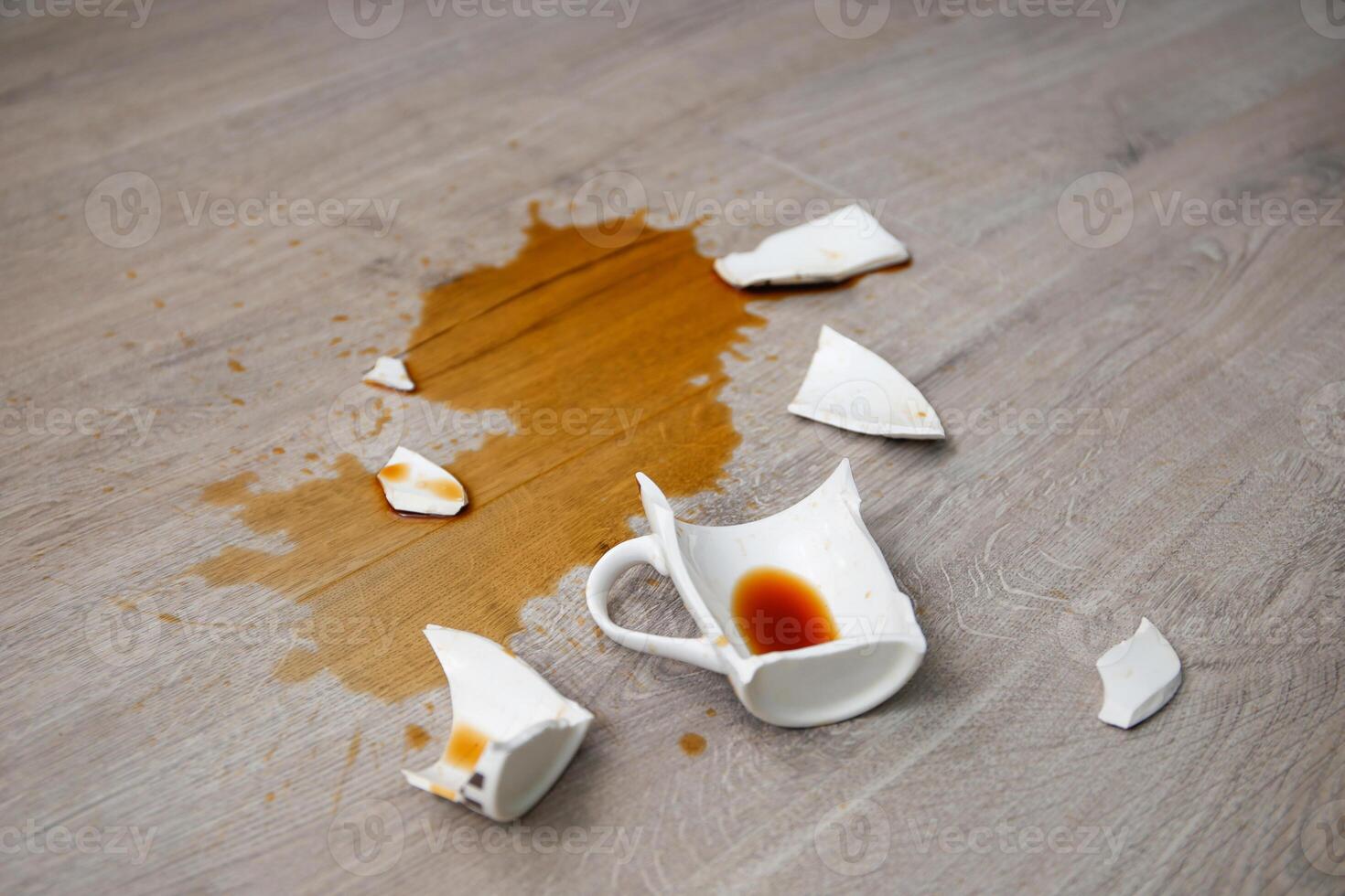 A broken cup of coffee fell on laminate, coffee spilled on floor. photo