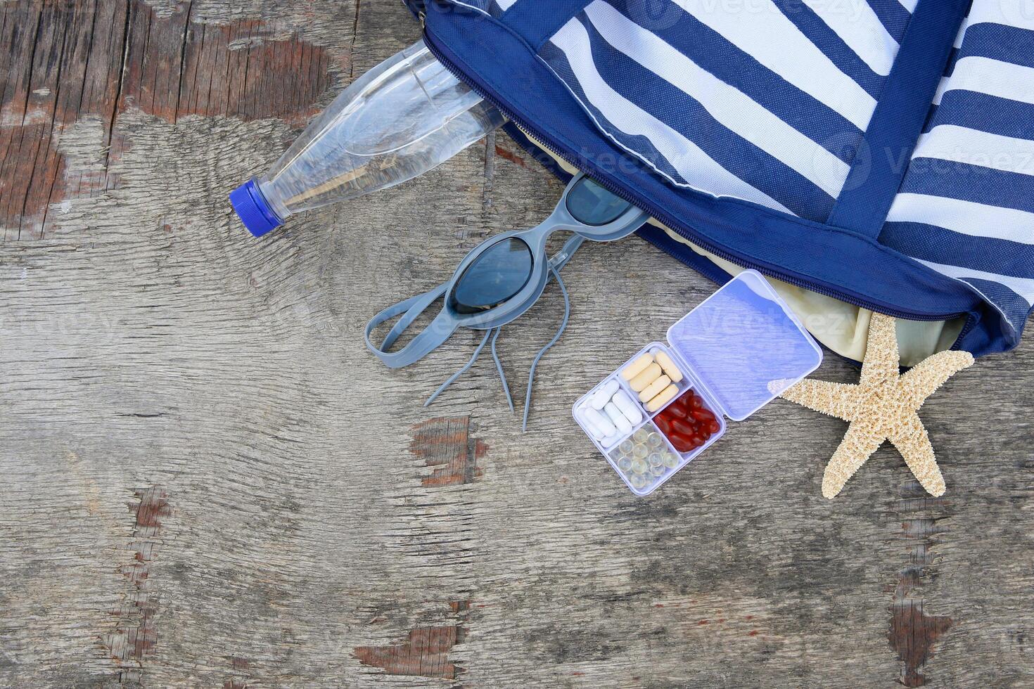 Summer women's beach accessories for your sea holiday and pill on old wooden background. Concept of medication required in journey. Top view. photo