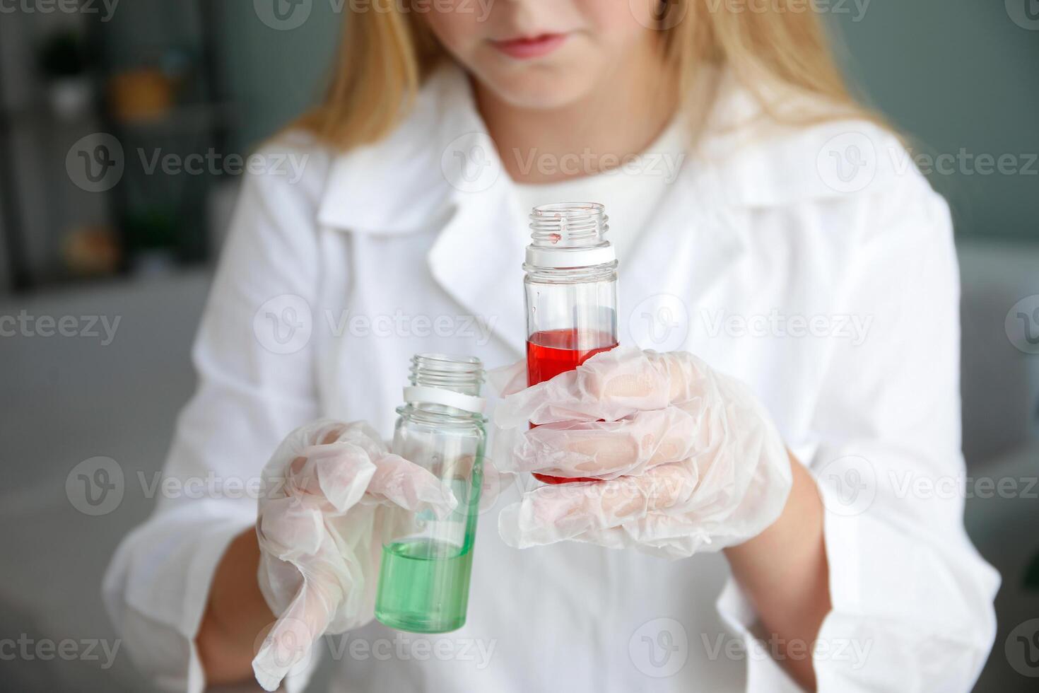 The girl conducts chemical experiments at home. Focus on flasks with colored liquid. photo