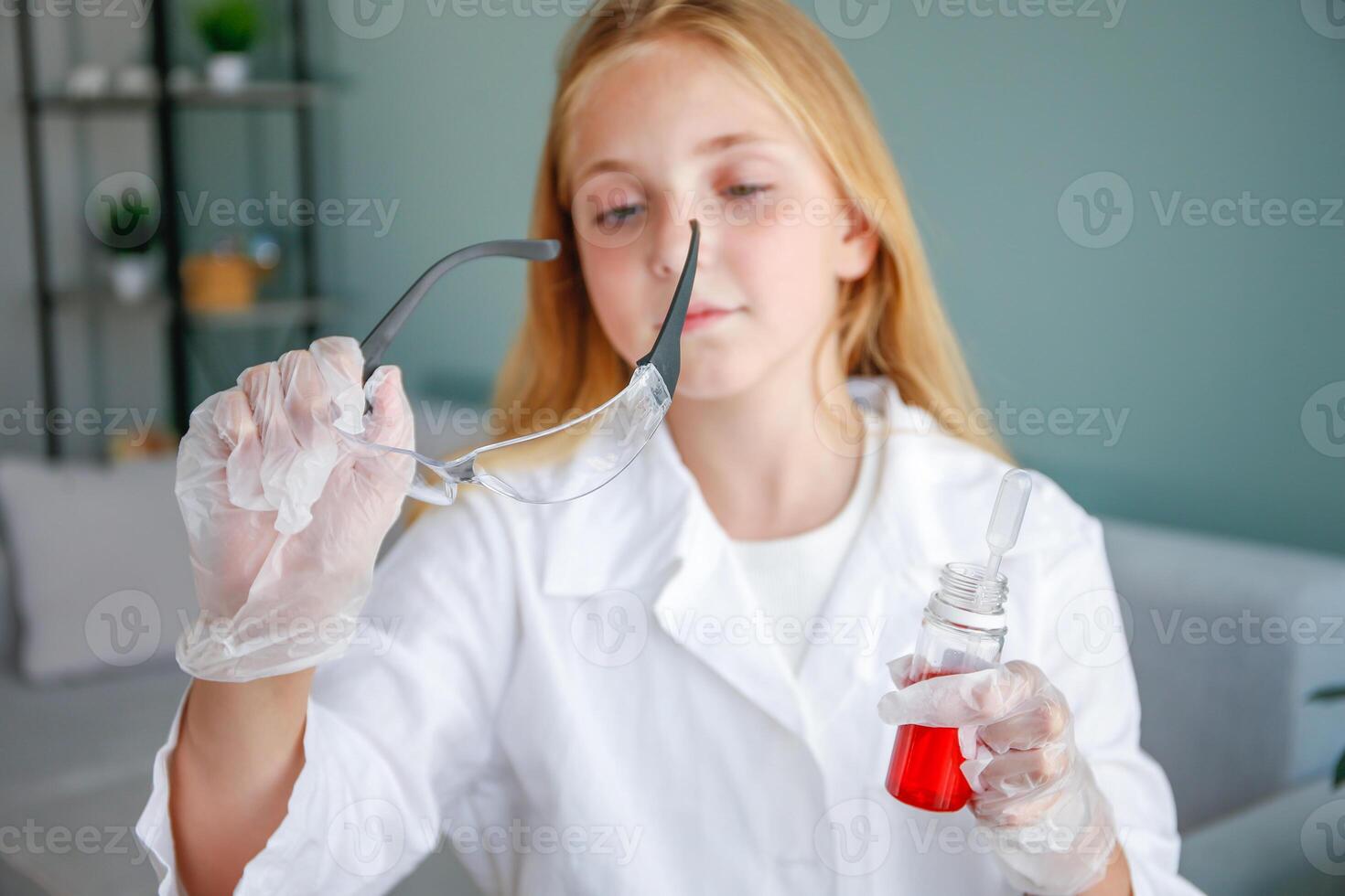 The girl conducts chemical experiments at home. Focus on flasks with colored liquid and glasses. photo