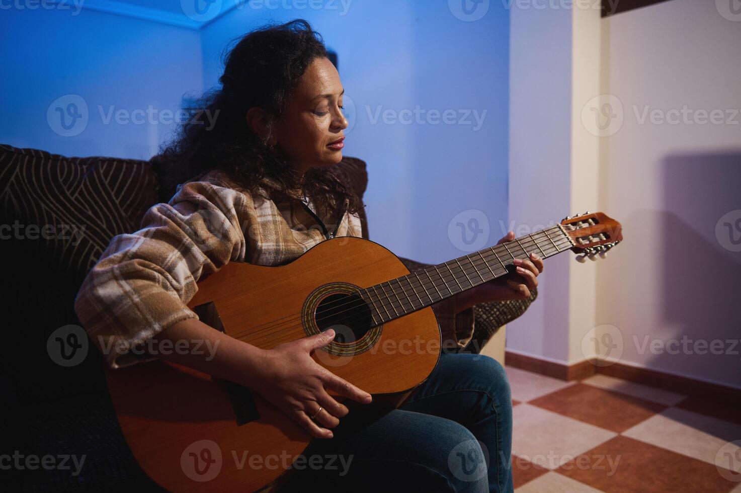 Woman enjoying playing guitar at home in cozy evening setting with focused expression photo