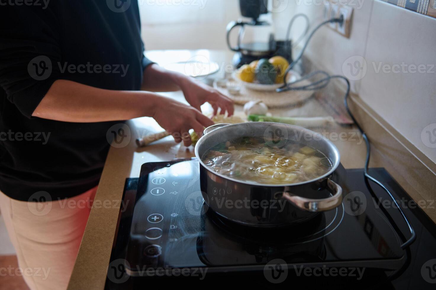 Person cooking soup on an electric stove with fresh ingredients photo