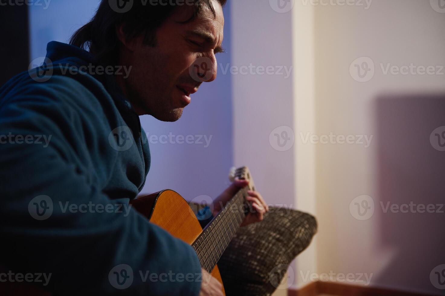 Man playing acoustic guitar with passion in a dimly lit room, expressing emotion and creativity through music photo