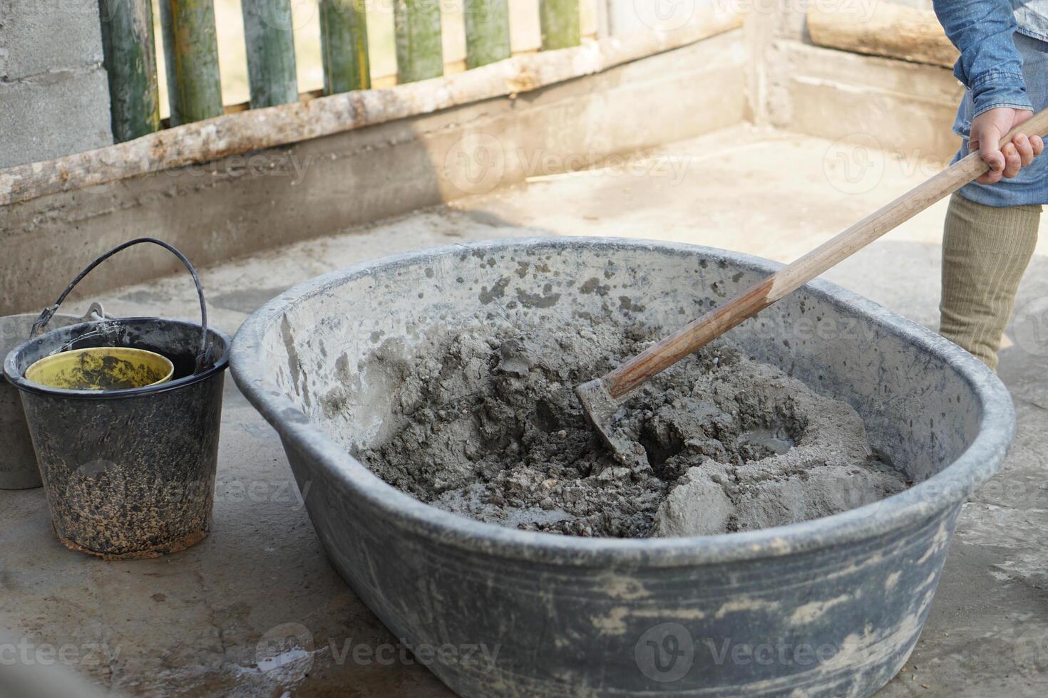 Close up worker using a hoe to mix cement powder, sand, stones in basin for mixing cement. Concept. Construction worker job. Hard working. Process of construction work with cement photo