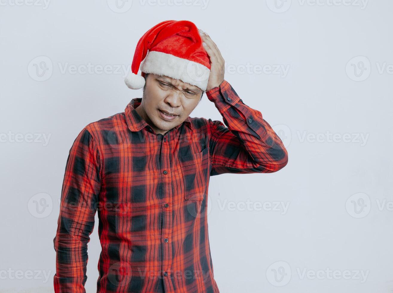 Young asian man wearing santa claus hat over isolated white background suffering from headache desperate and stressed because pain and migraine. Hands on head. photo
