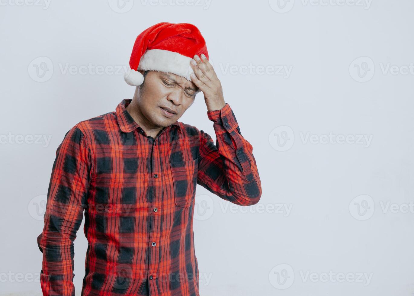 Young asian man wearing santa claus hat over isolated white background suffering from headache desperate and stressed because pain and migraine. Hands on head. photo