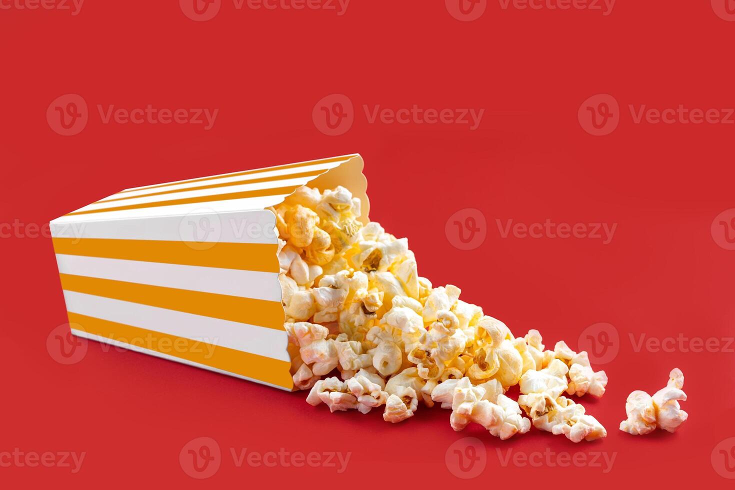 Tasty cheese popcorn falling out of a yellow striped carton bucket, isolated on red background photo