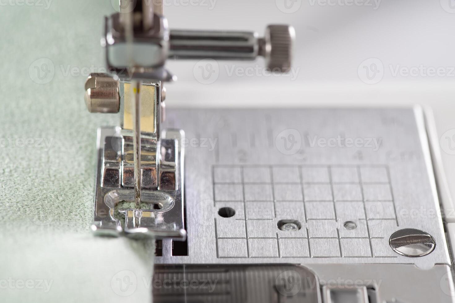 Modern sewing machine presser foot with green fabric and thread, closeup, macro photo