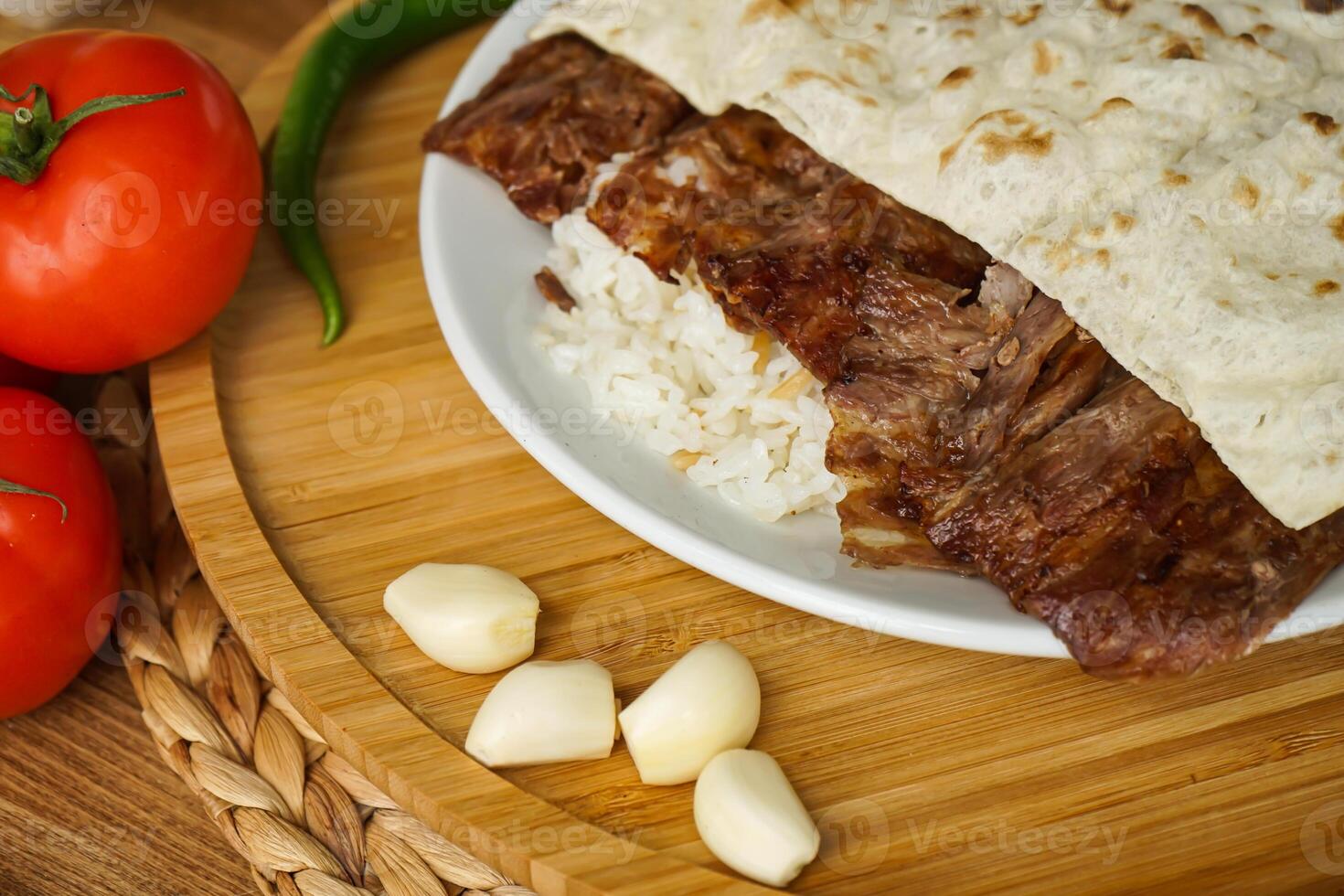 Meat Doner Kebab on Rice portion and Pita Bread served in plate with garlic, tomato, and green chilli isolate on wooden board closeup side view of arabic and turkish fast food photo